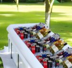 Two white BCWATERFUNPD inflatable serving bars filled with ice, drinks, and snacks at an outdoor party setting.