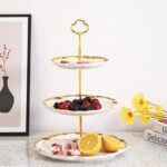Elegant BPFY 3-tier porcelain serving tray with gold trim and embossed floral design, holding cupcakes and pastries.