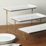 Three-tier serving set with white rectangular plates and a gold metal stand, displaying various snacks.