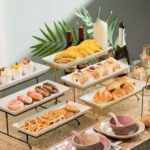 A three-tier Gomakren serving stand with gold frame and white rectangular porcelain platters, displaying various desserts.