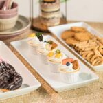 A three-tier Gomakren serving stand with gold frame and white rectangular porcelain platters, displaying various desserts.